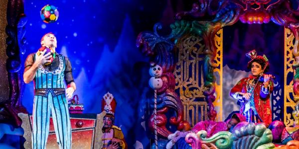 Un momento del circo con un giocoliere che lancia palline colorate, mentre un'artista suona il violino in un ambiente festoso e colorato